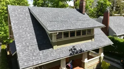 Gray shingled roof of a house with a green facade and a small porch.