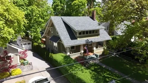 Two-story green house with a dark gray roof, surrounded by trees and a hedge.