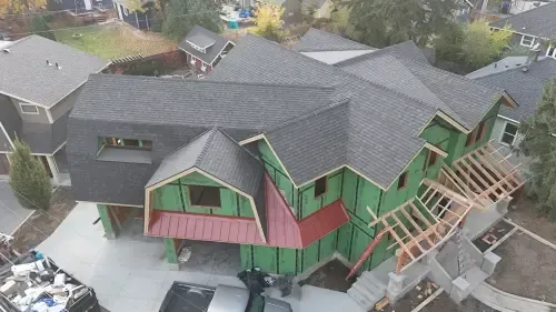 Aerial view of a house under construction with a dark gray roof and exposed green siding.