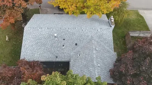 Overhead view of a house with a gray shingle roof, surrounded by fall foliage of red, yellow, and green.