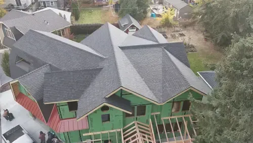 House under construction, green framing, dark gray roof, wood trim, unfinished, aerial view.