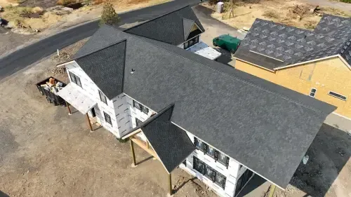 Aerial view of a house with a dark gray shingled roof, under construction, set in a dry, outdoor environment.