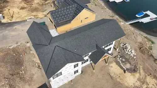 Aerial view of a two-story house with a dark gray roof near a lake and dock.