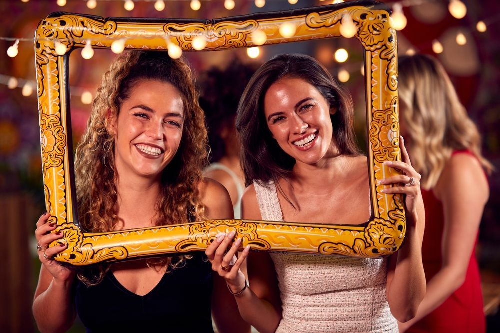 Two women are holding an inflatable picture frame at a party.