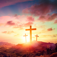 Three crosses on top of a hill at sunset.