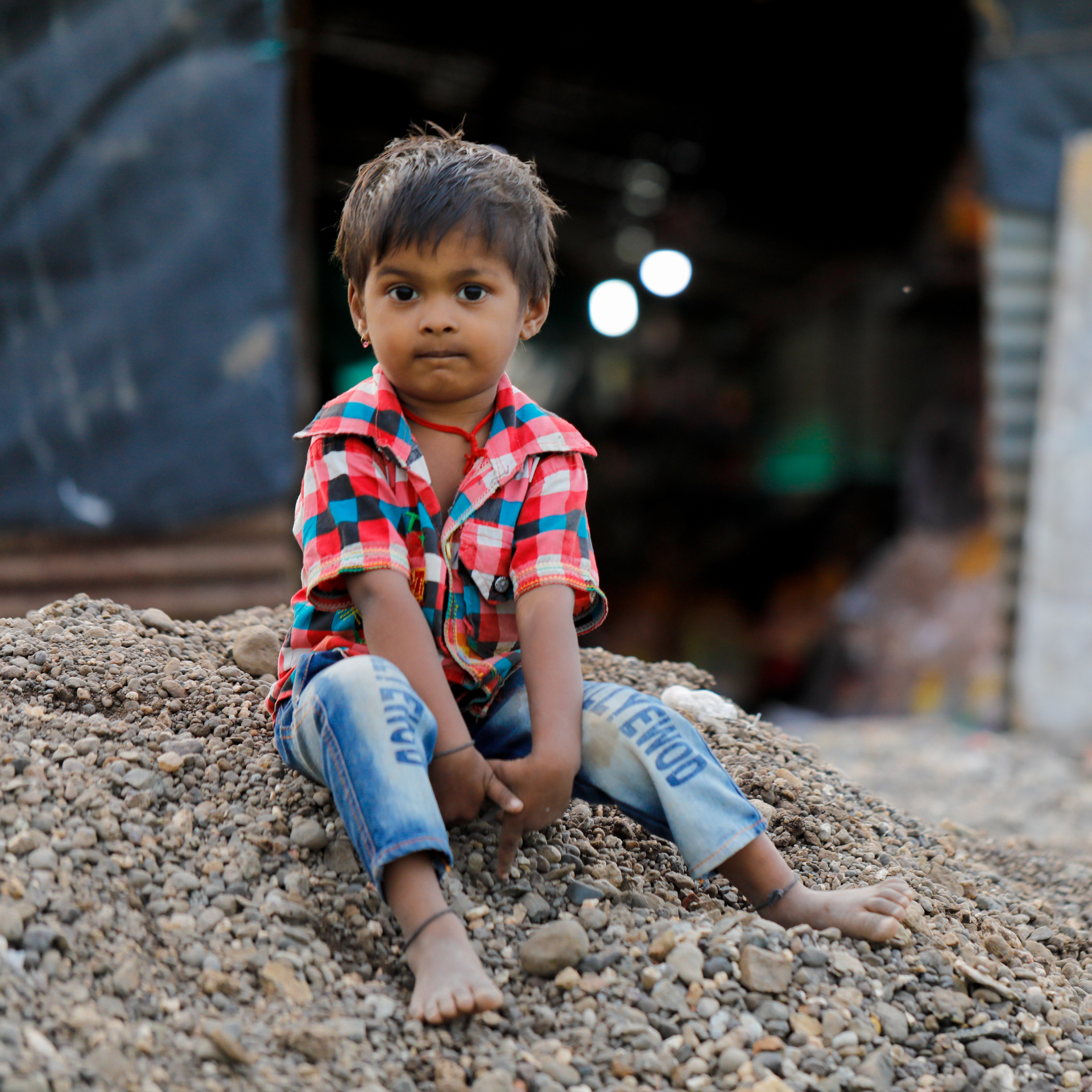 A young boy is sitting on a pile of rocks with the word denim on his jeans