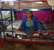 An elderly woman is sitting in a bunk bed.SUn