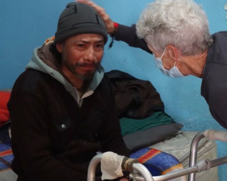 A man wearing a beanie is being helped by a woman wearing a mask