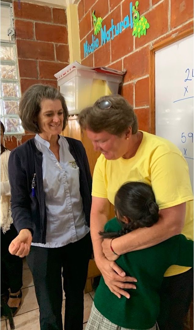 A woman in a yellow shirt is hugging a child in a classroom.