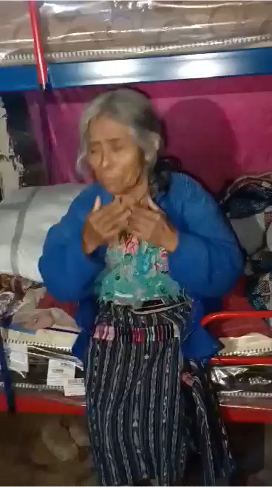 An elderly woman is sitting on a bench eating a piece of food.