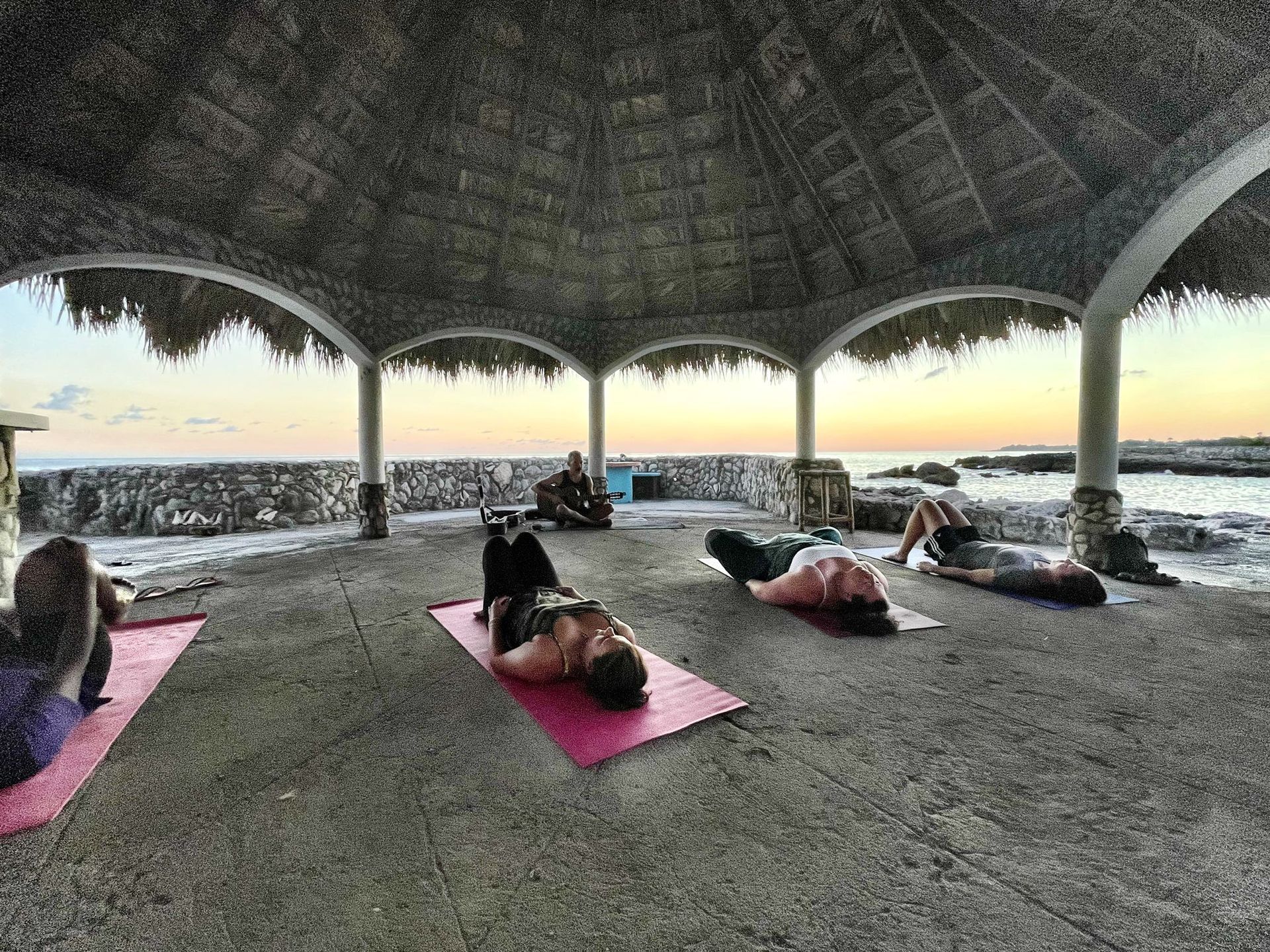 A group of people are doing yoga under a thatched roof.