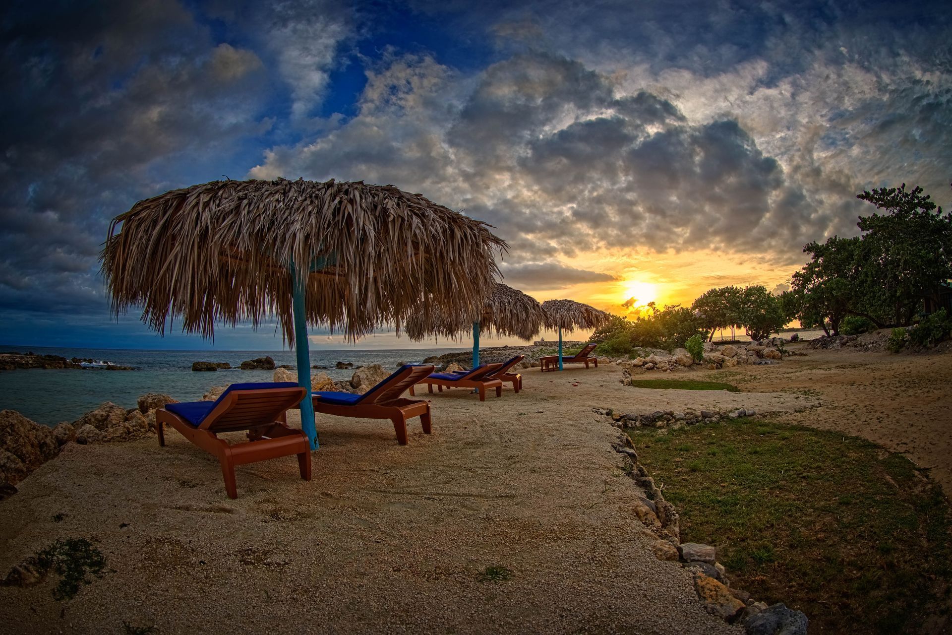 There are umbrellas and chairs on the beach at sunset.