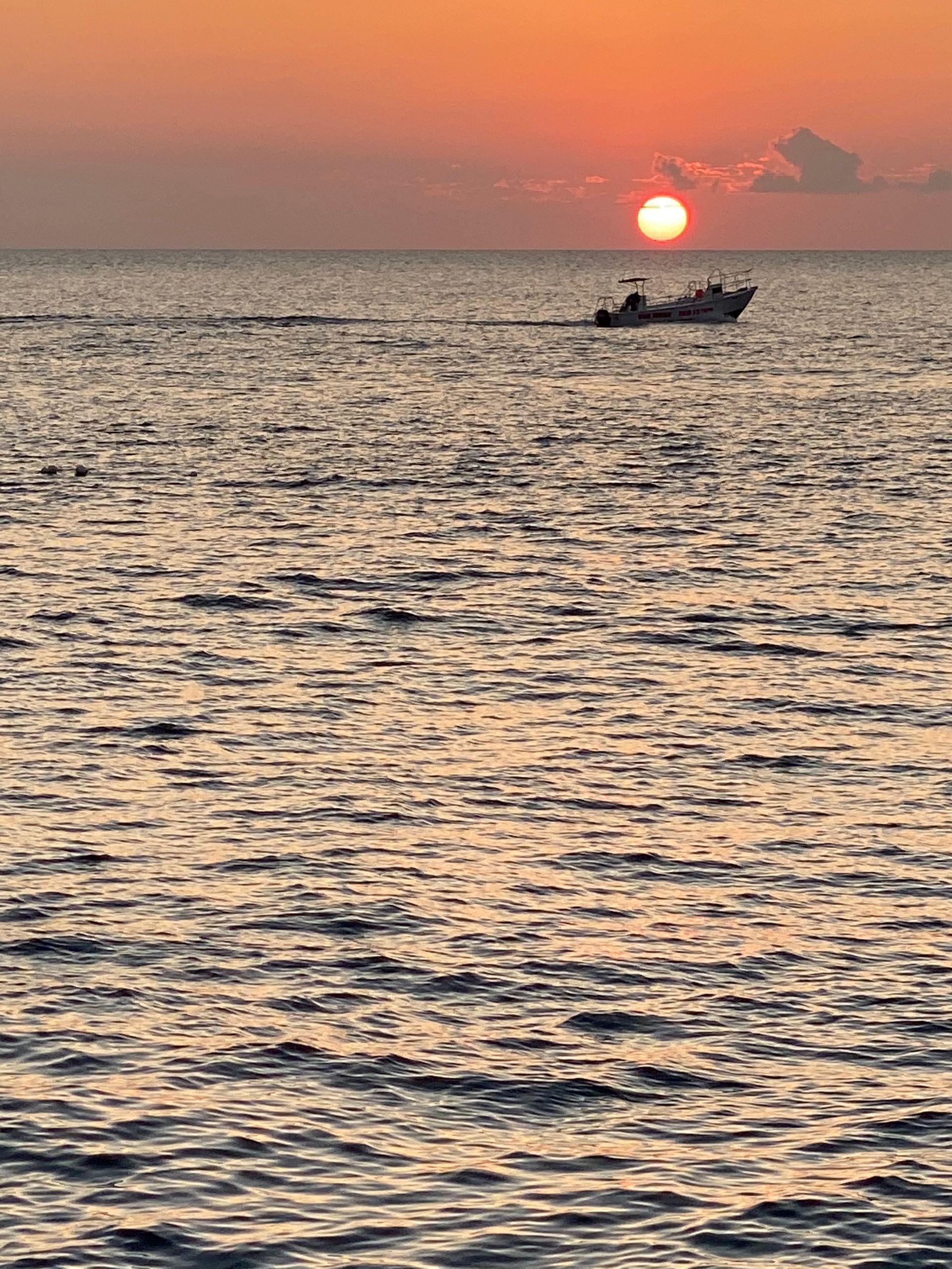 A boat is floating in the ocean at sunset.