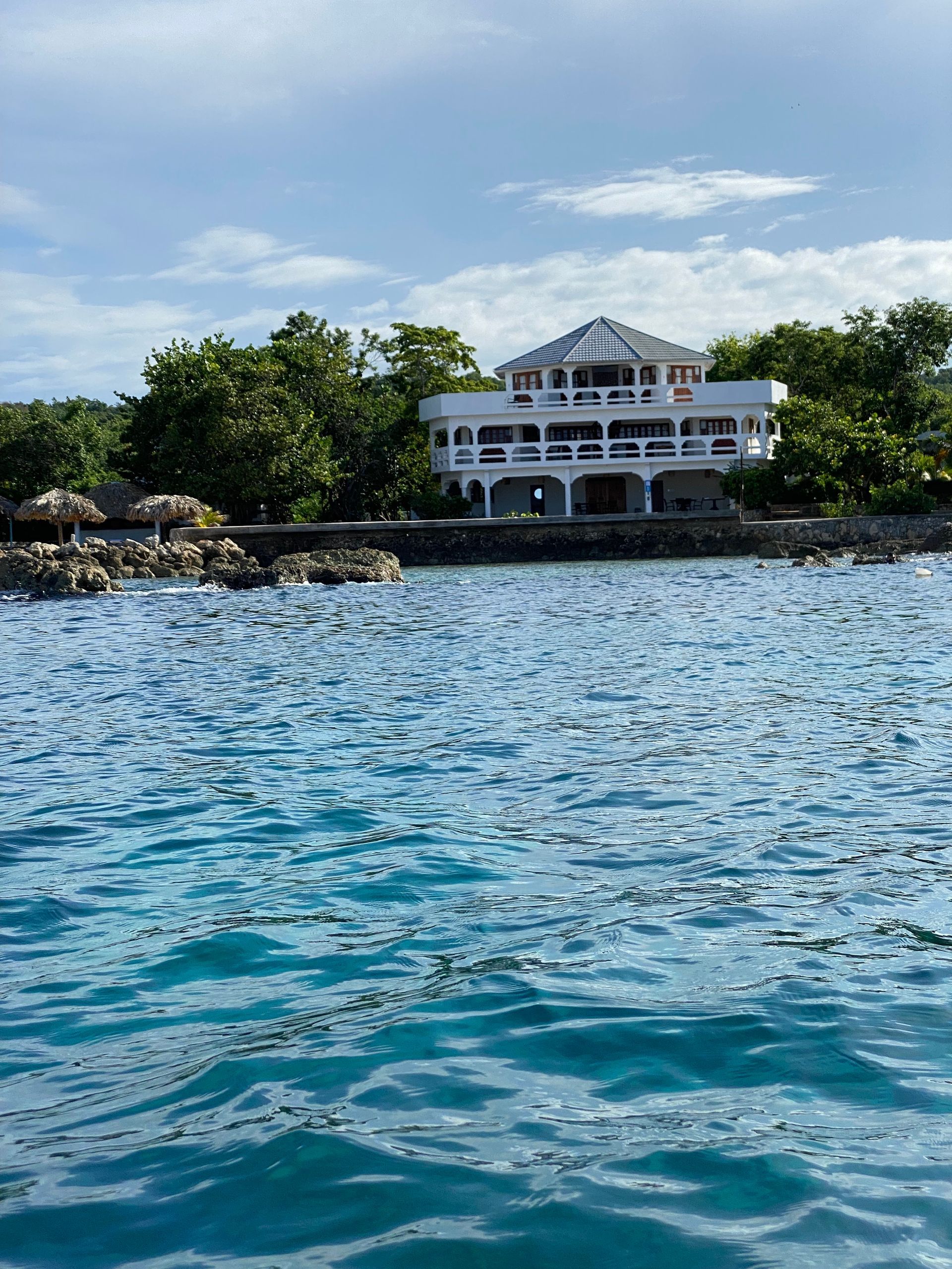 A large white house is sitting on a small island in the middle of the ocean.