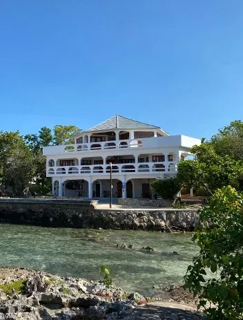 A large white house sits next to a body of water
