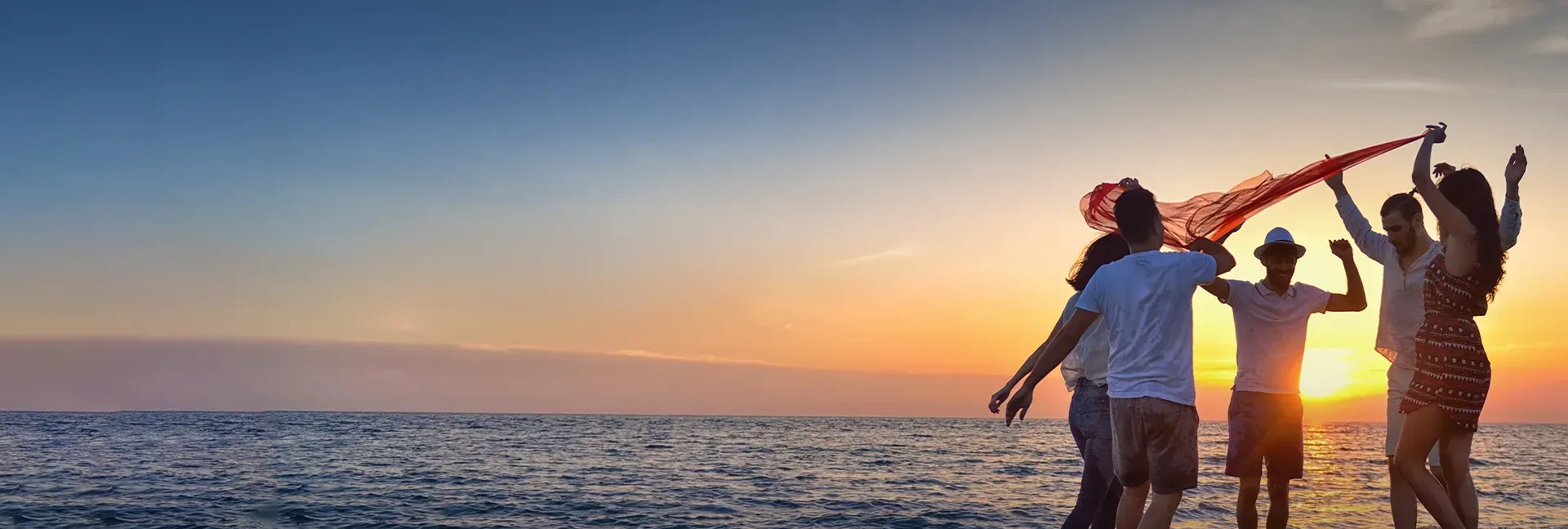 A group of people are standing on a beach at sunset.
