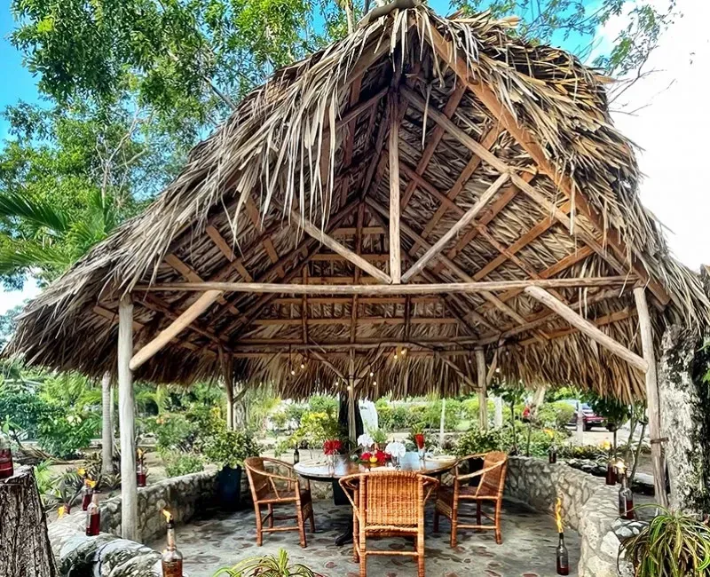 A thatched gazebo with a table and chairs underneath it.