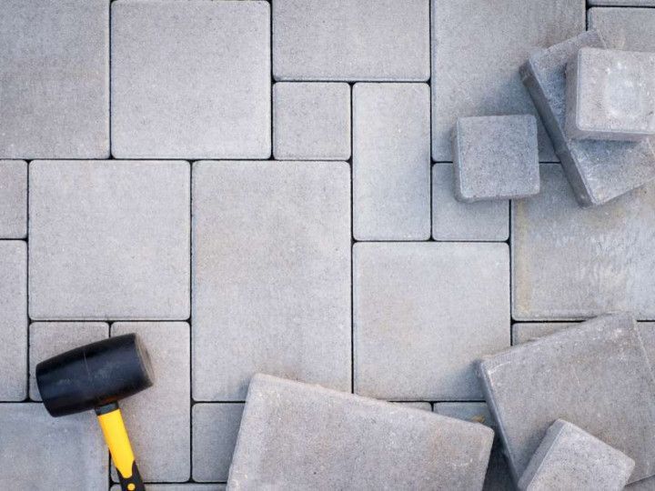 A gray outdoor dining table and bench set with a beige umbrella on a white patio rug, located on a stone pool deck.