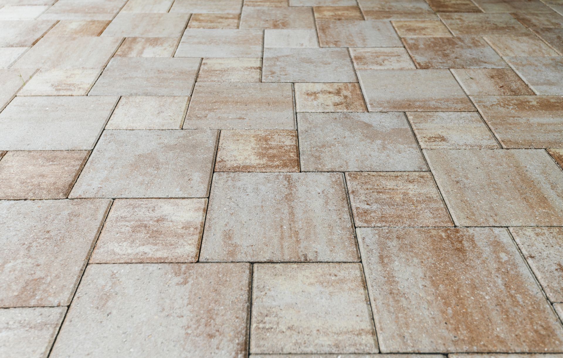 A close-up view of stone patio pavers in varying shades of tan, beige.