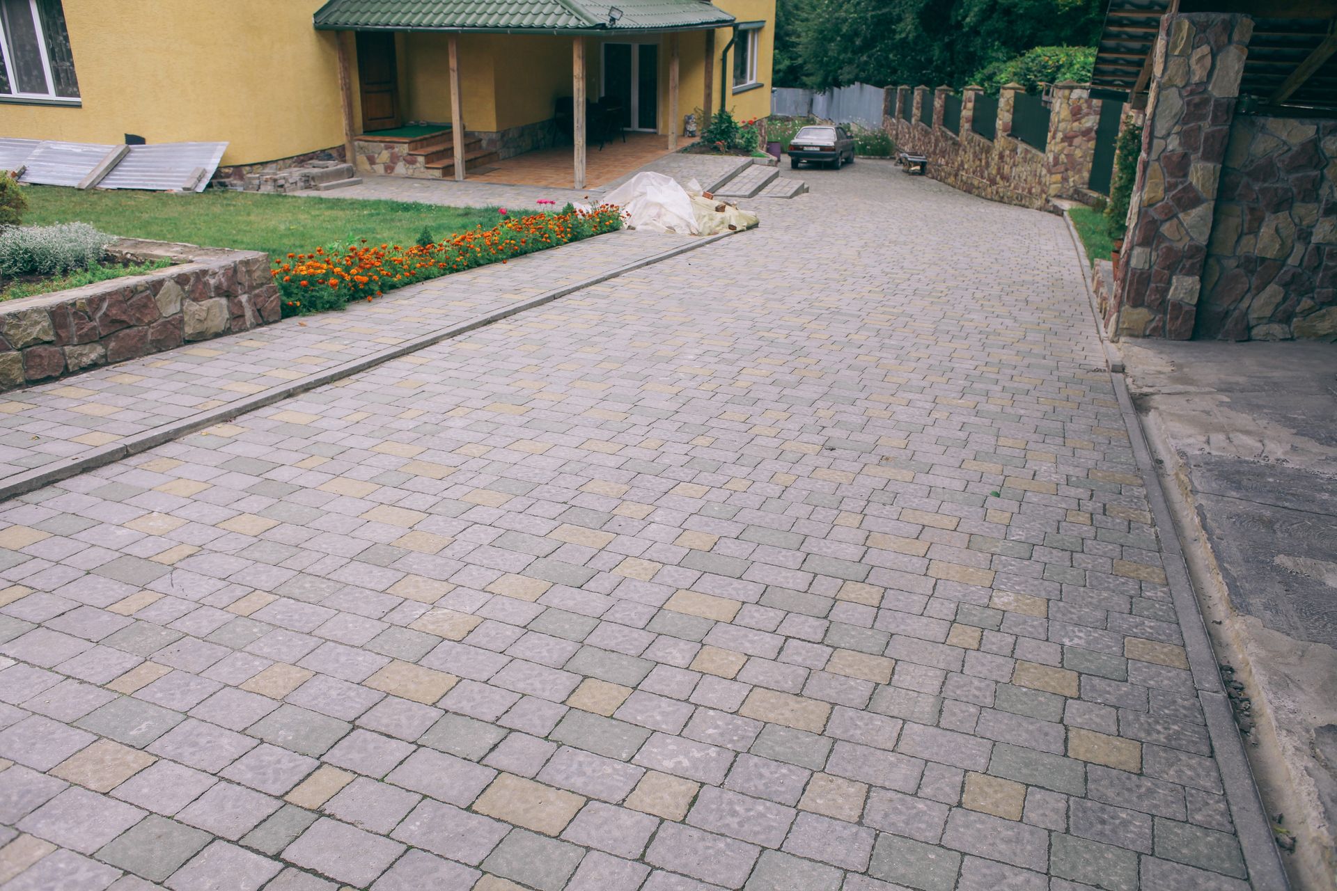 A paved driveway made of multi-colored stone bricks leading toward a house entrance with a green porch.