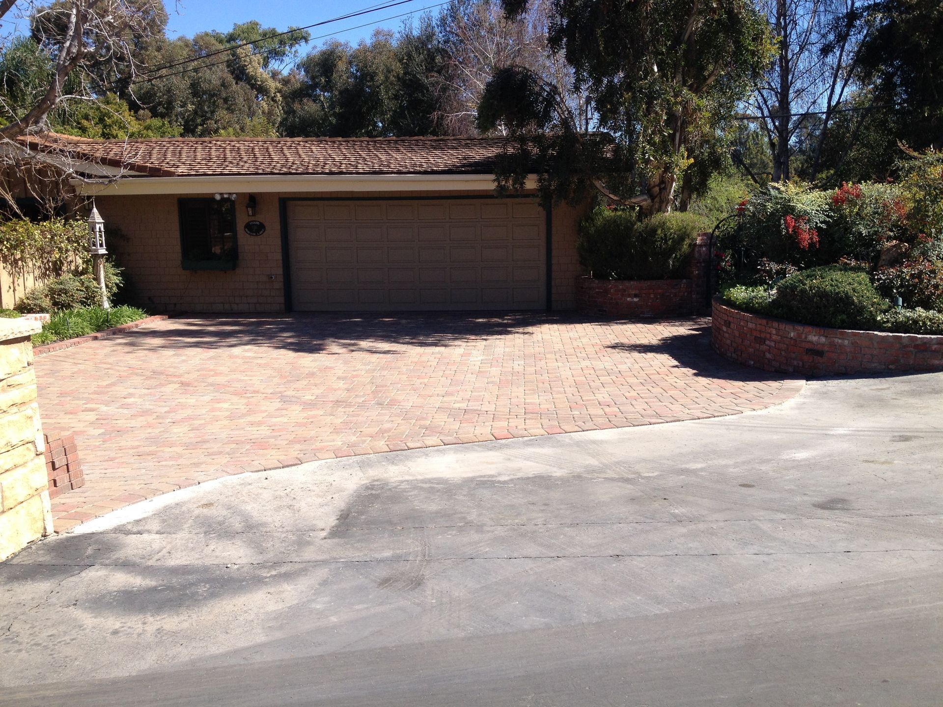 A beige garage with a tiled roof features a tan paver driveway.
