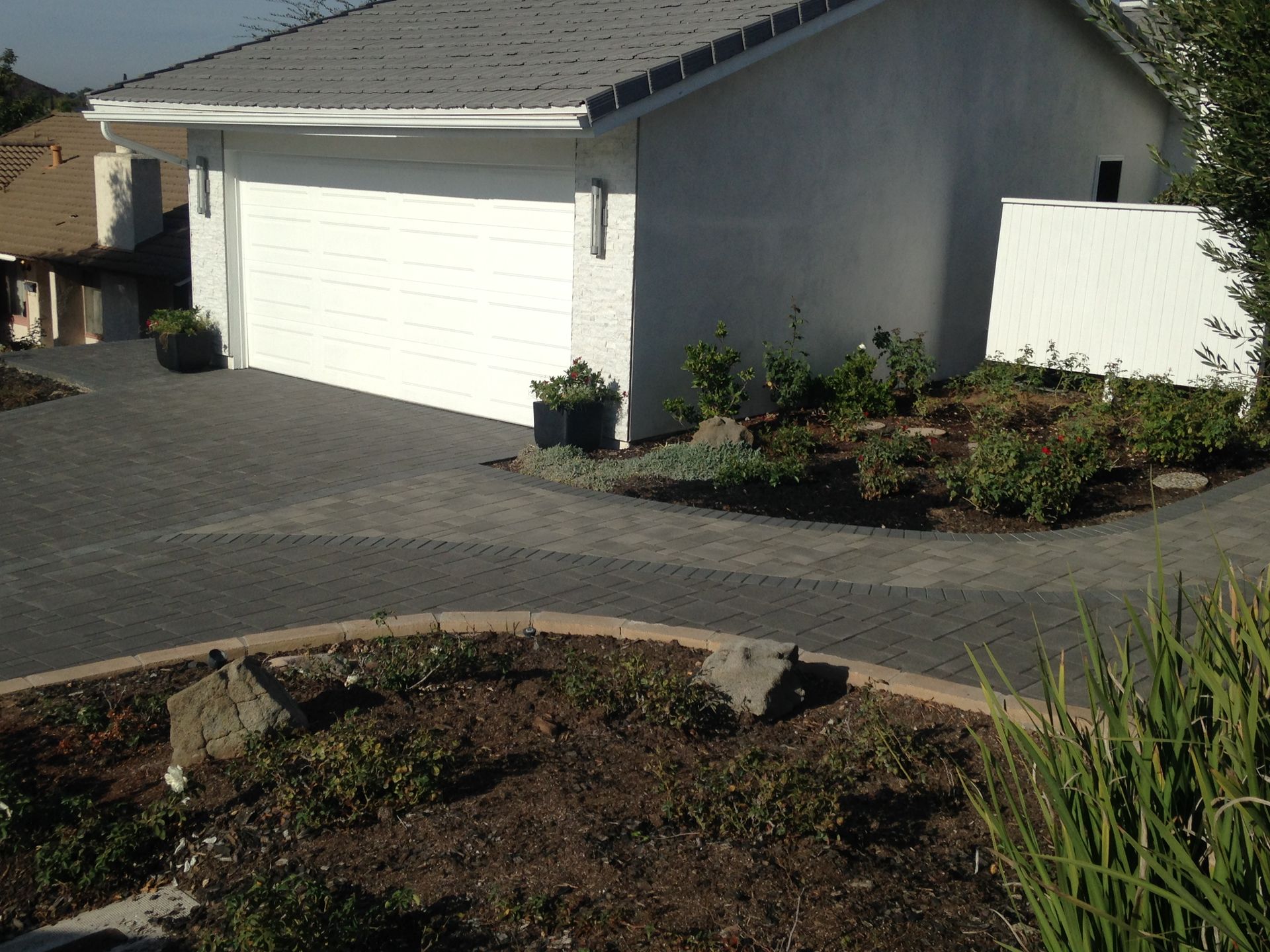 A white garage with a gray paver driveway and a garden bed in the foreground.
