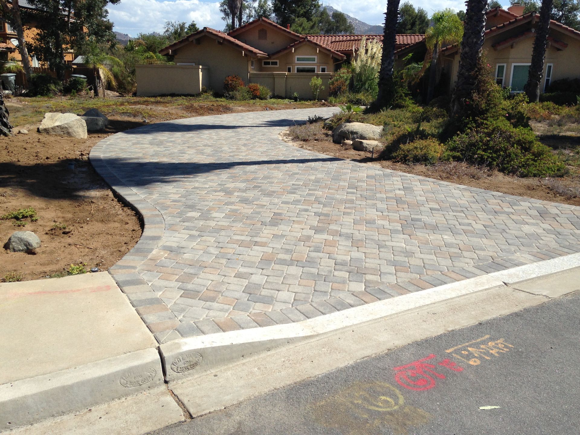 A curved paver driveway connects to a concrete curb and asphalt road in front of a residential home.