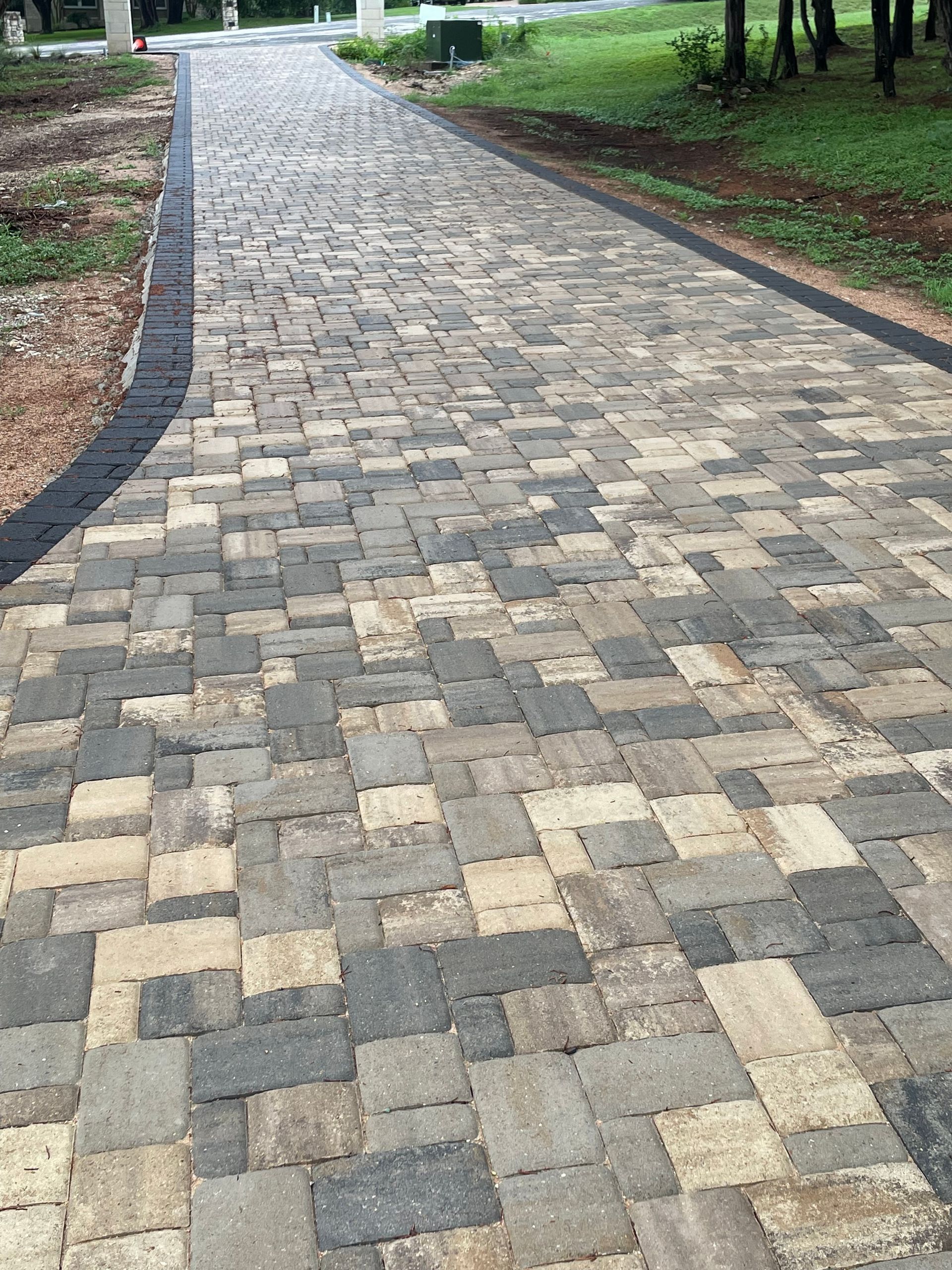 A pathway made of rectangular interlocking pavers in shades of tan.