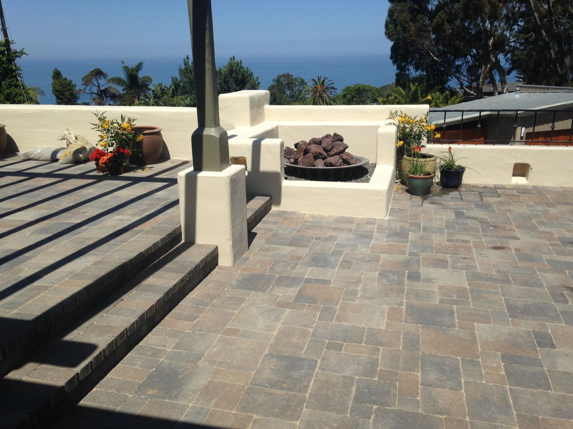 A tiled patio with a stone fire pit, potted plants.