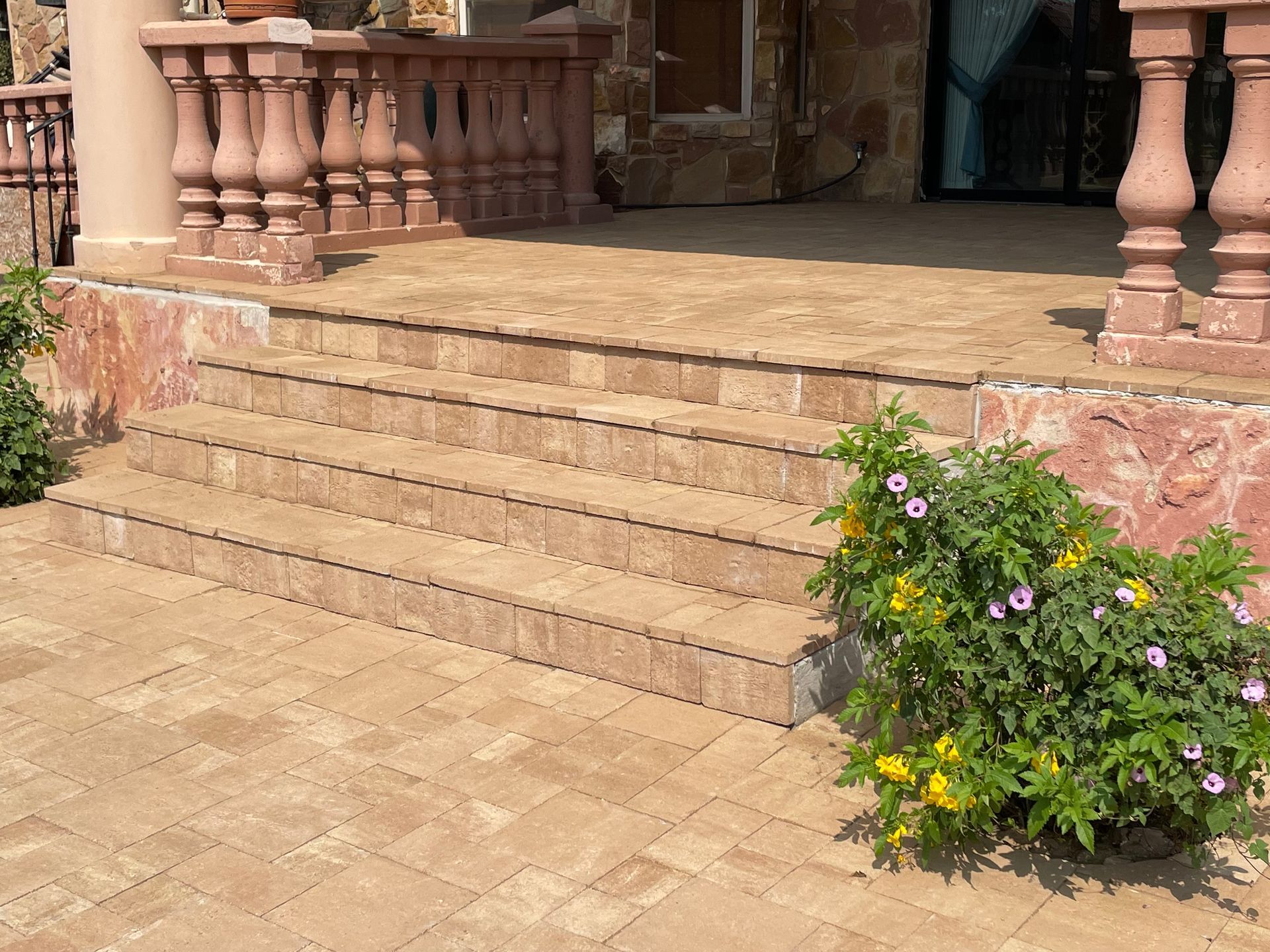 Stone steps leading to a tiled patio with a stone balustrade and a flowering bush in the foreground.