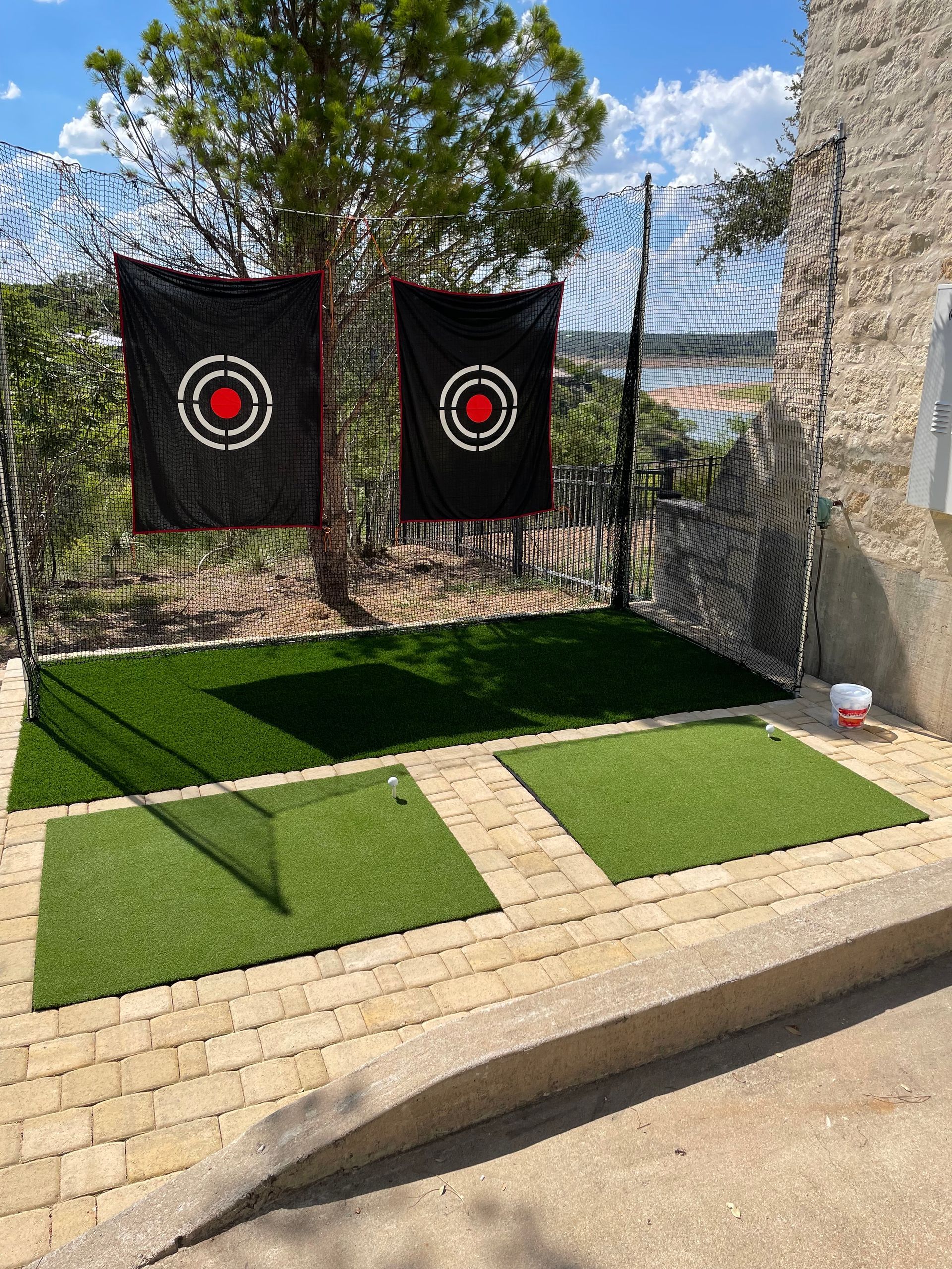 An outdoor golf practice area with two target nets hanging in front of artificial turf mats on a patio.