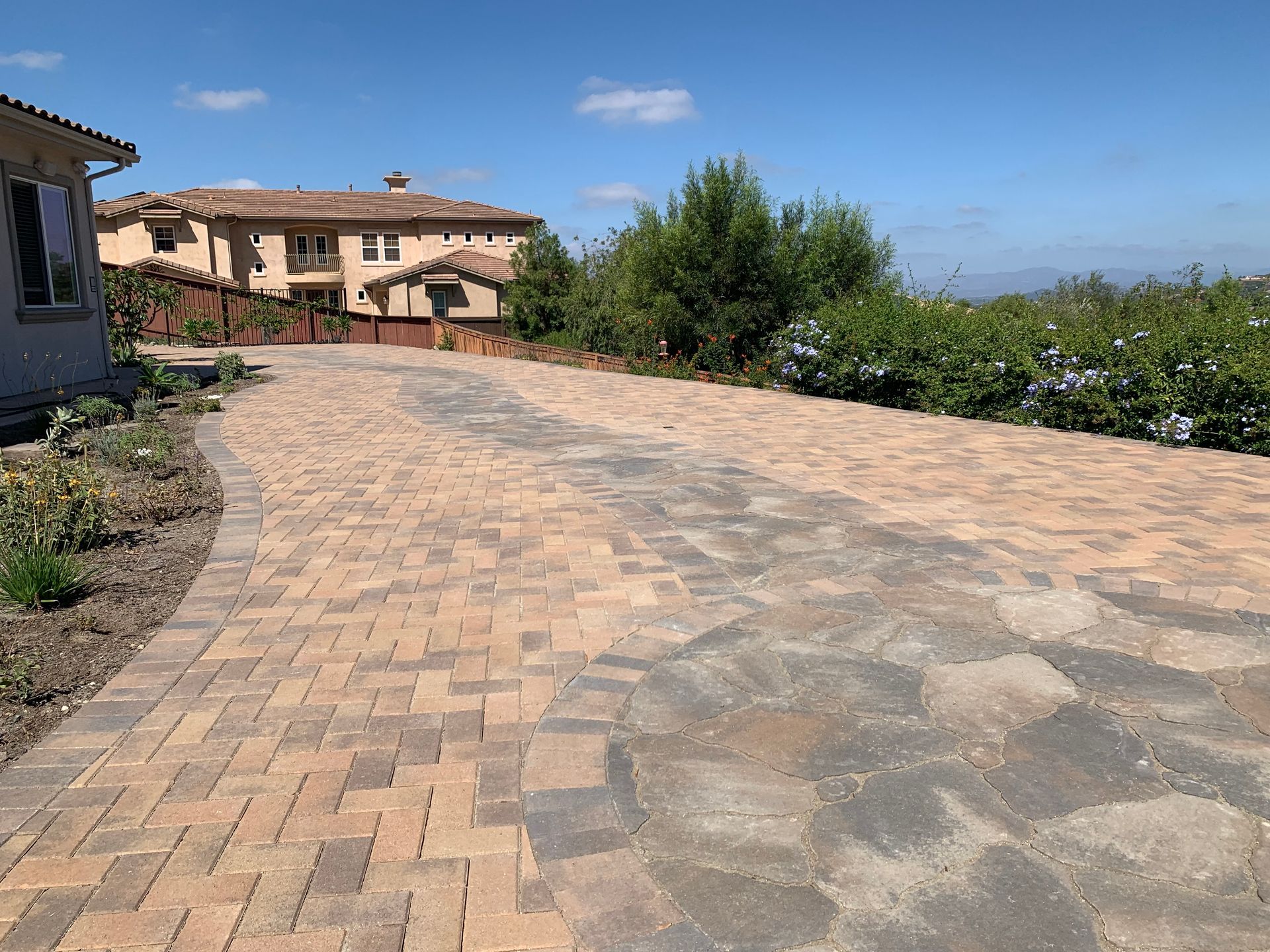 A long driveway paved with beige herringbone bricks and gray stone.