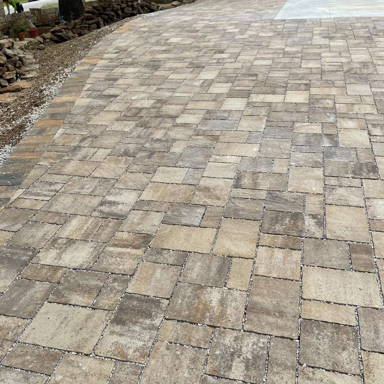 A driveway or patio paved with rectangular stones in varying shades of tan.