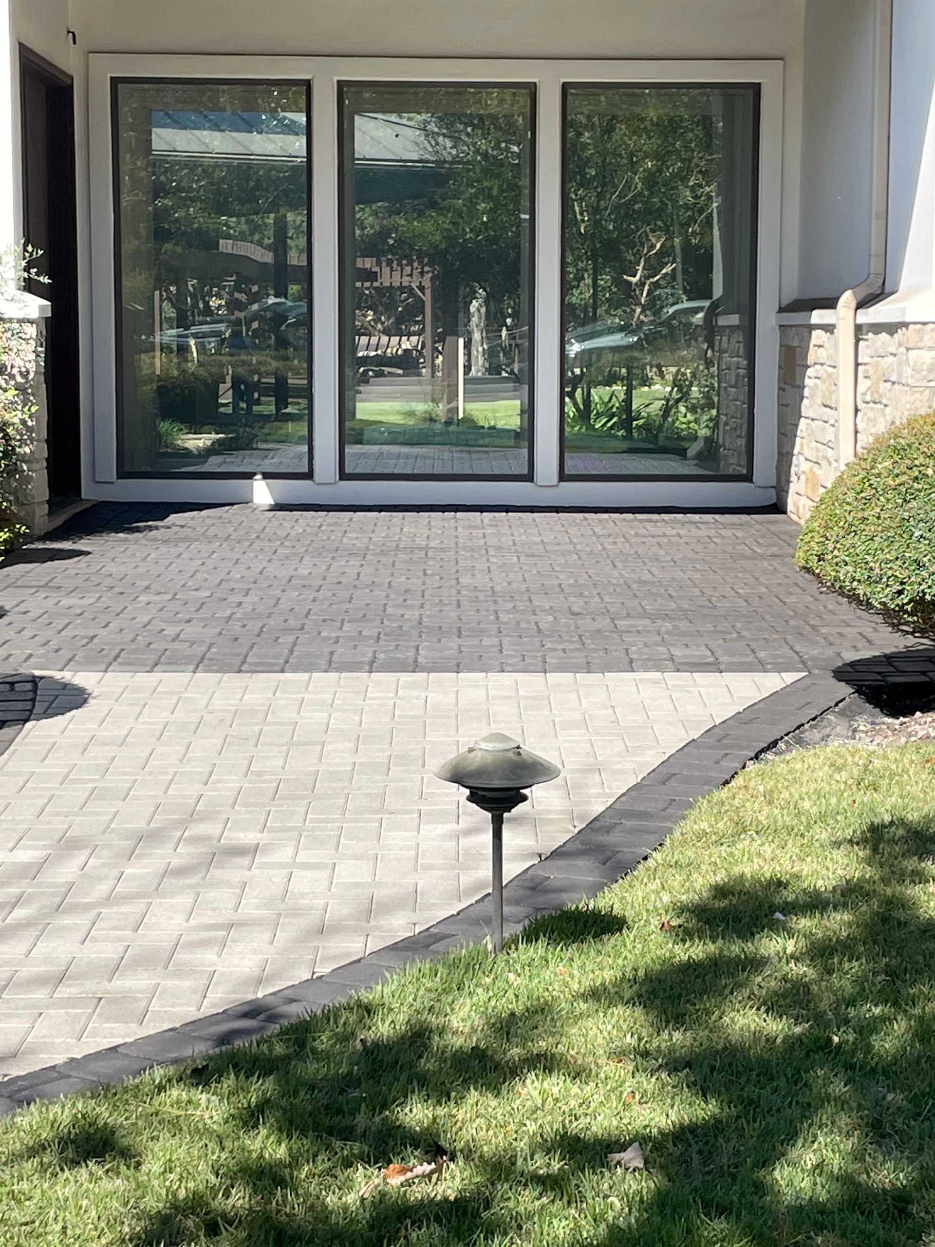 A patio with dark and light gray pavers leading to a large glass door.