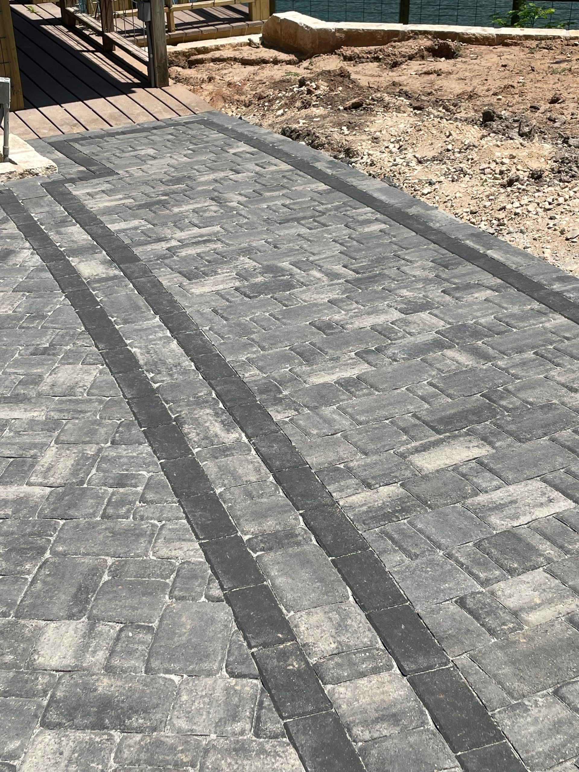 A patio of gray, multi-sized rectangular pavers with two parallel black border lines running across the surface.