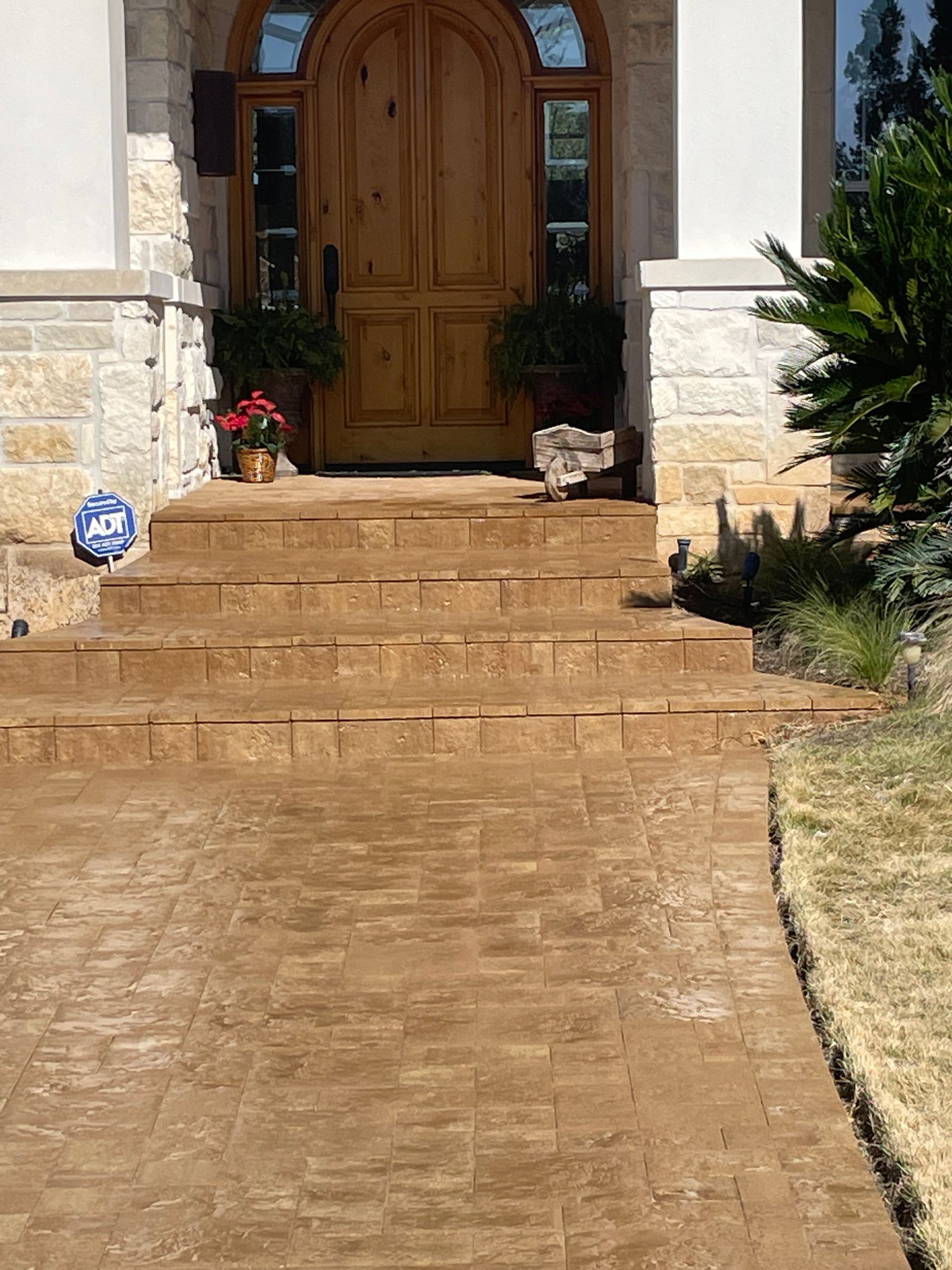 A brick-paved walkway leading to three stone steps and an arched wooden front door of a stone-accented home.