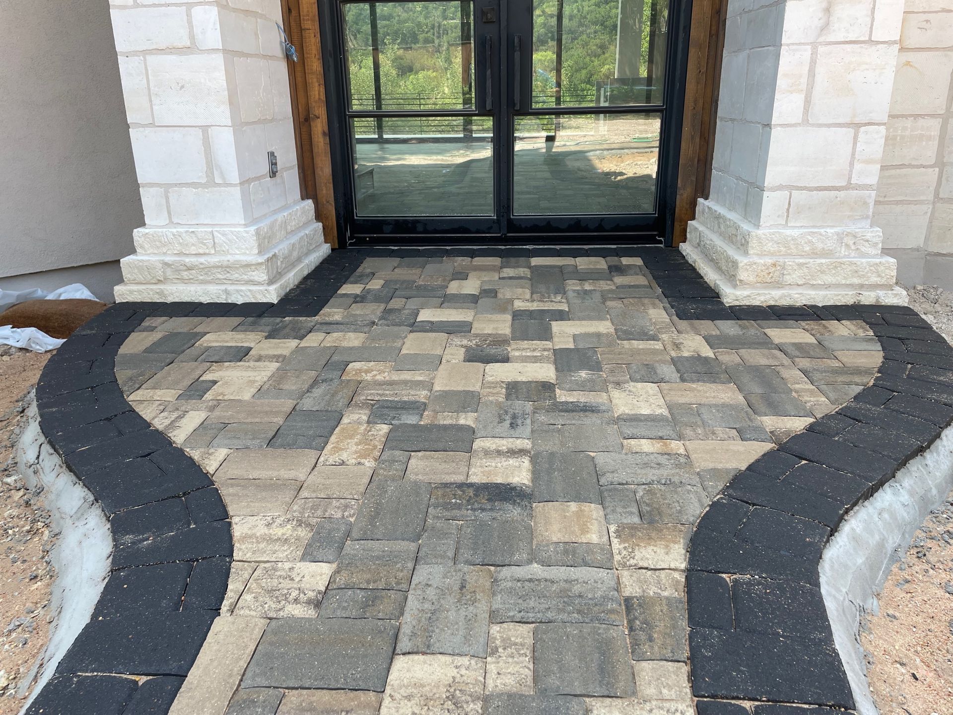 A front entryway with a decorative stone paver walkway featuring a tan and gray pattern bordered by dark charcoal bricks.