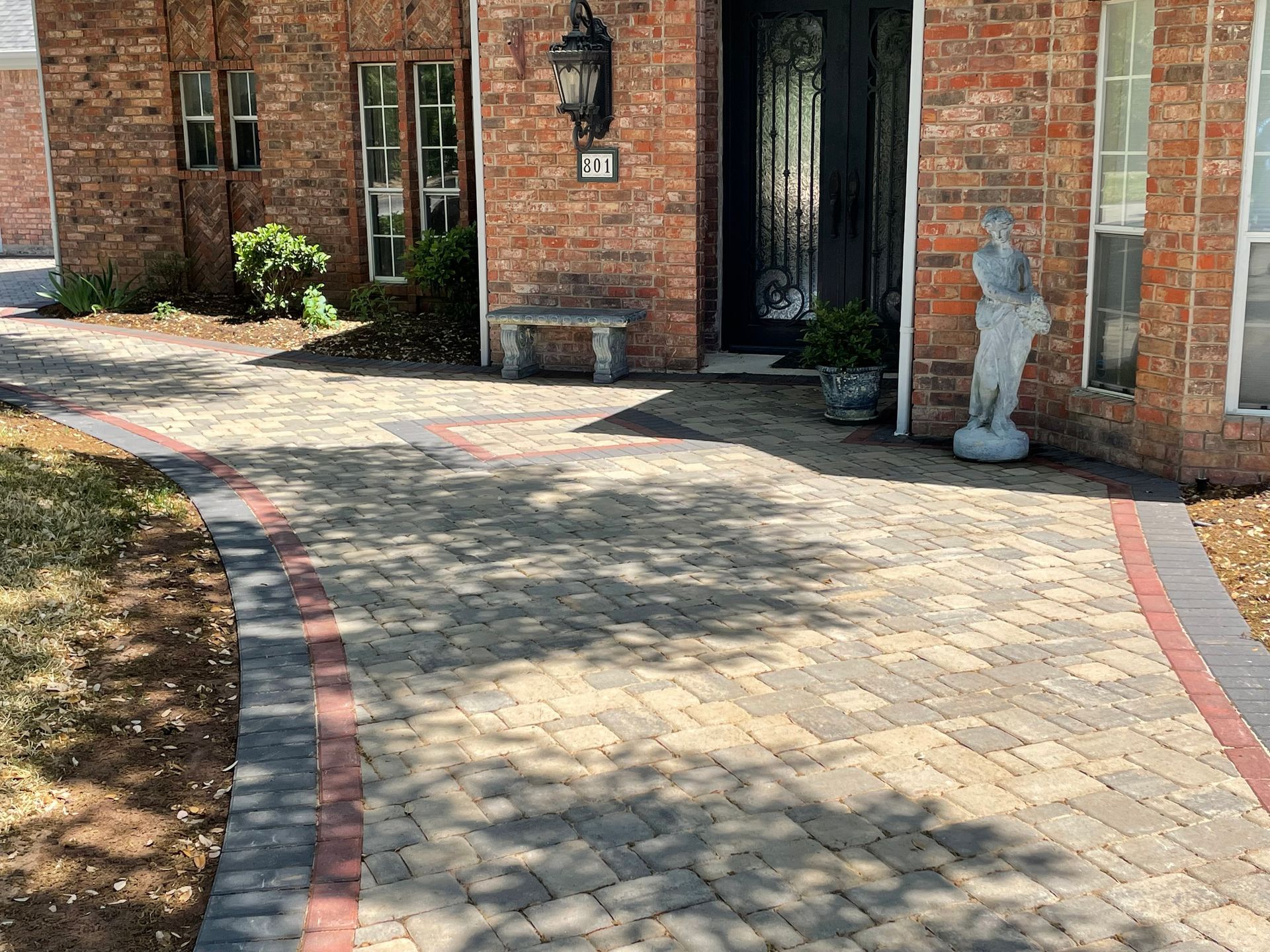 A paved brick walkway leads to a red brick house entrance featuring a dark double door and a small stone statue.