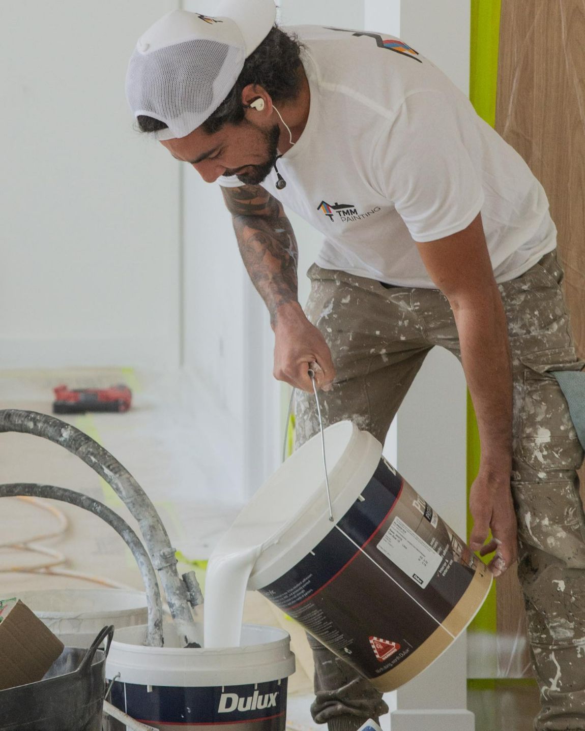 A Man is Pouring White Paint Into a Bucket That Says Dulux — TMM Painting in Main Beach, QLD