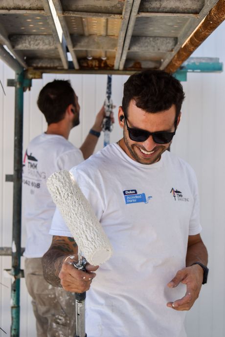 Two men are painting a wall and one is holding a paint roller