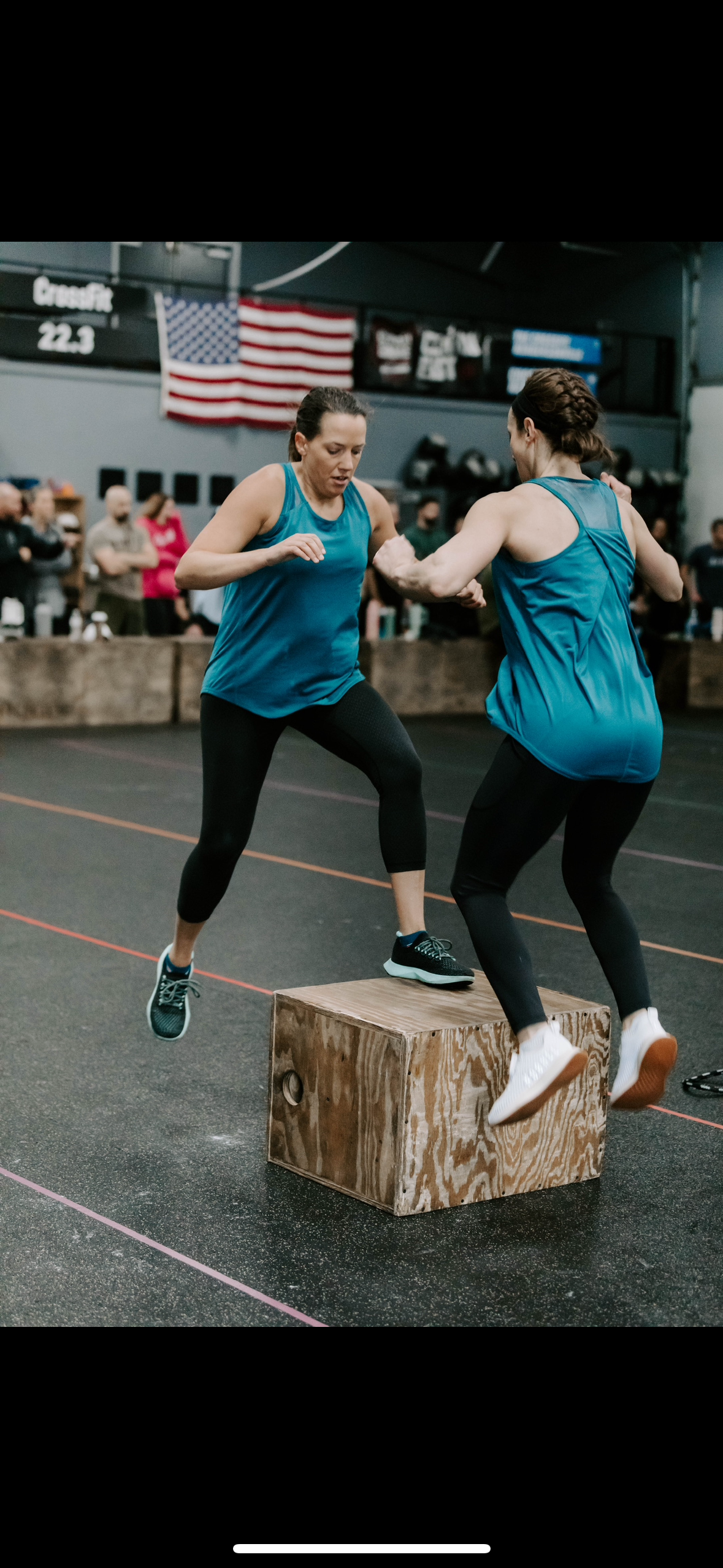 Two women are jumping over wooden blocks in a gym.