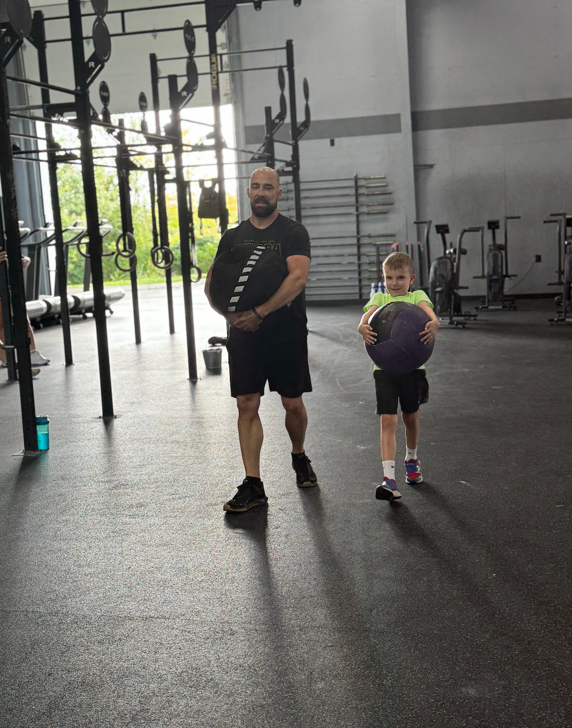 A man and a child are standing in a gym holding a ball.