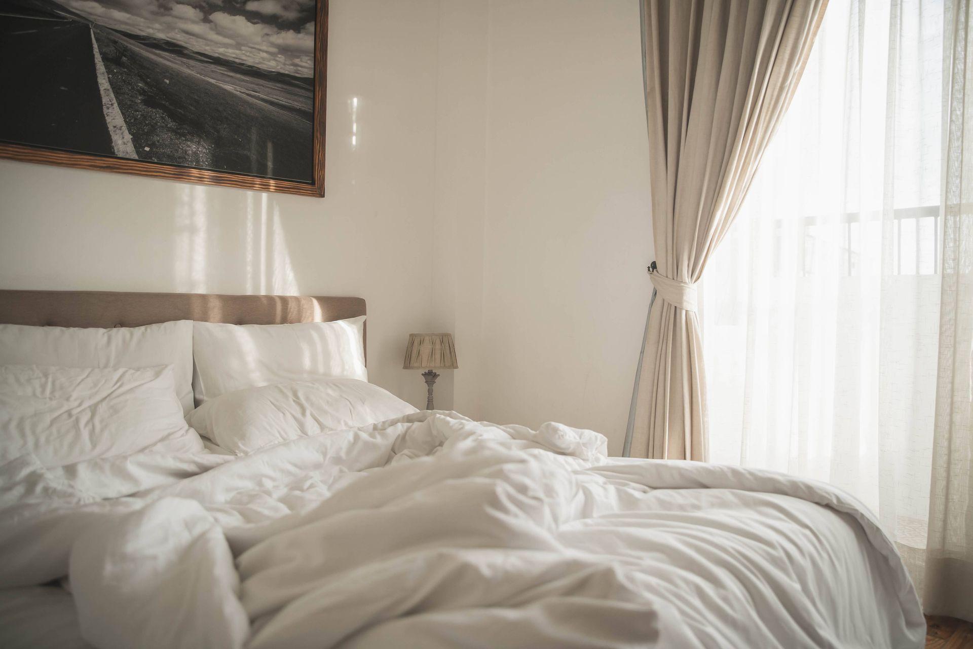 A cozy bed beside layered window coverings for bedrooms with morning light streaming inside