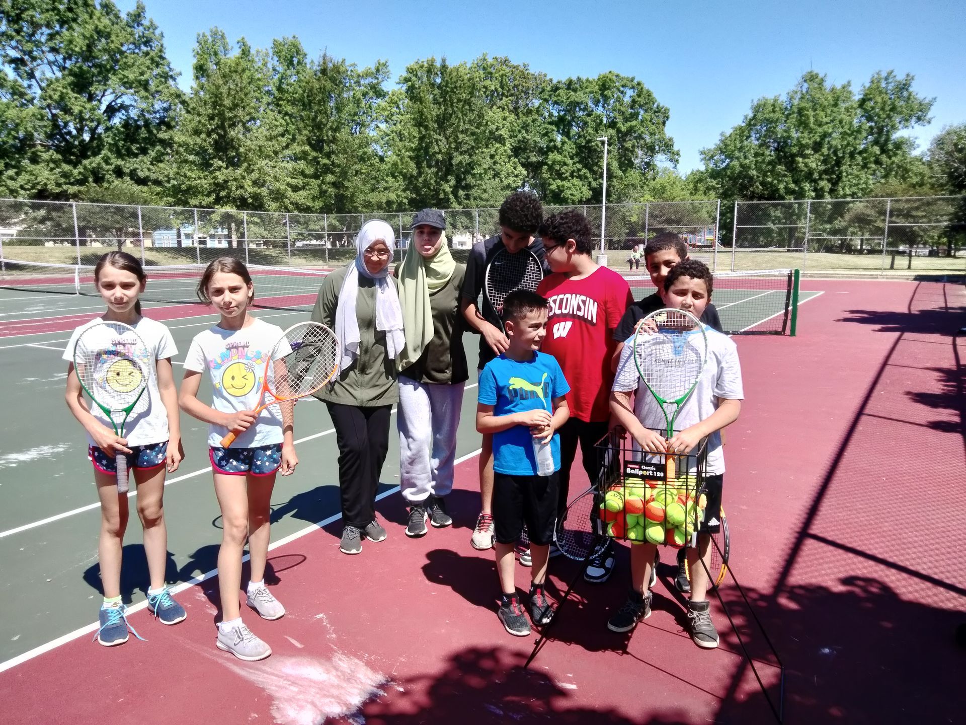 A group of children standing on a tennis court holding tennis rackets