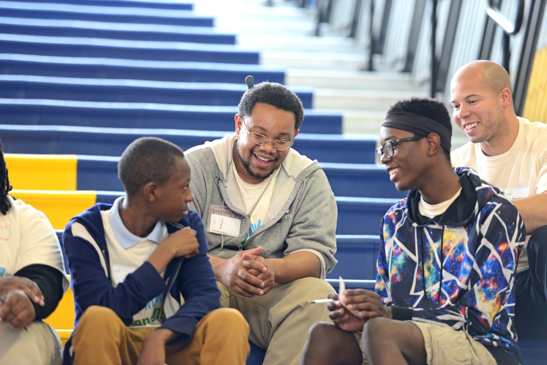 A group of young men are sitting on a set of stairs talking to each other.