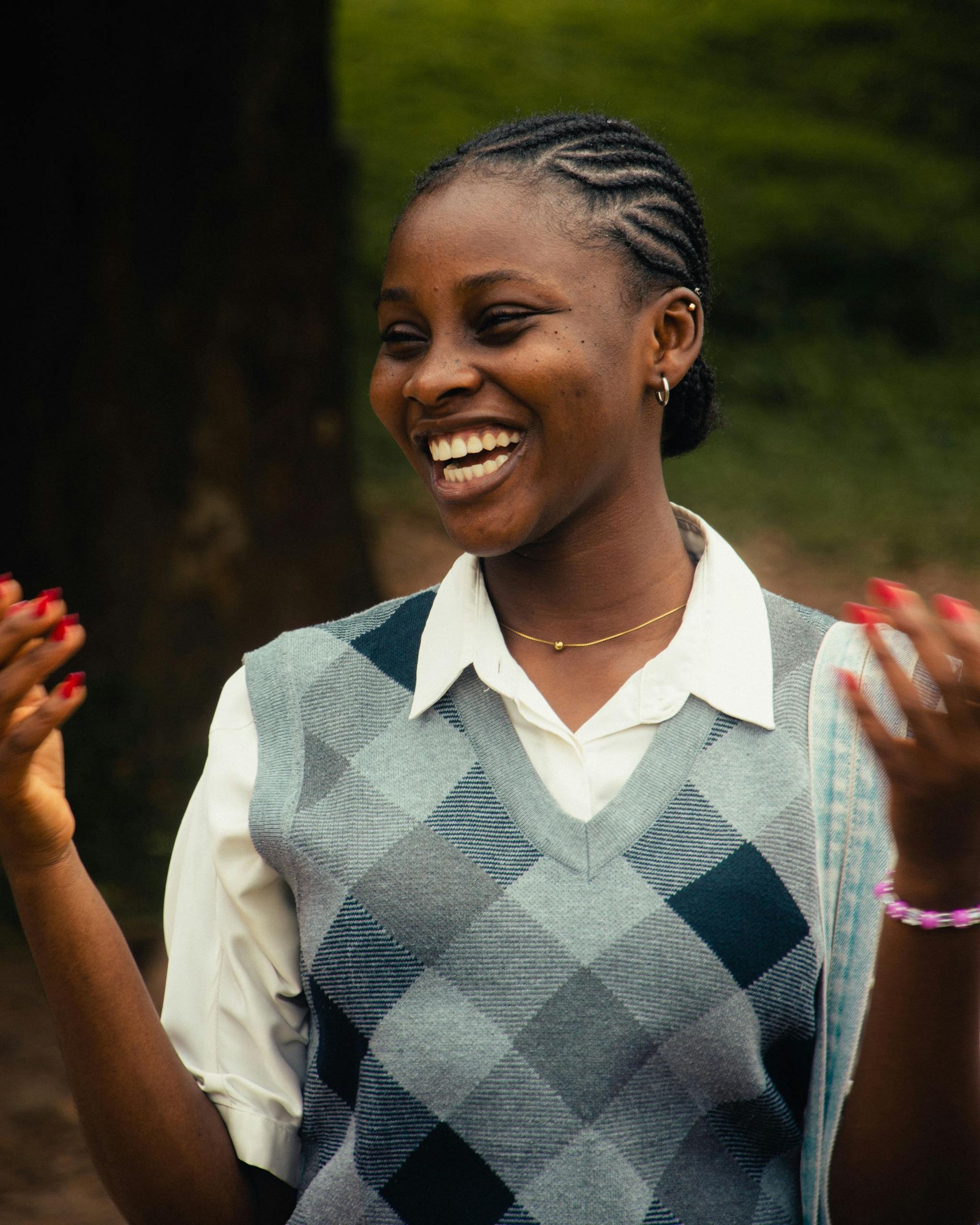 Smiling woman in a gray plaid vest, braids, and white shirt outdoors.
