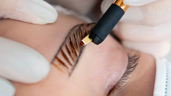 A woman is getting her eyebrows tattooed with a machine.
