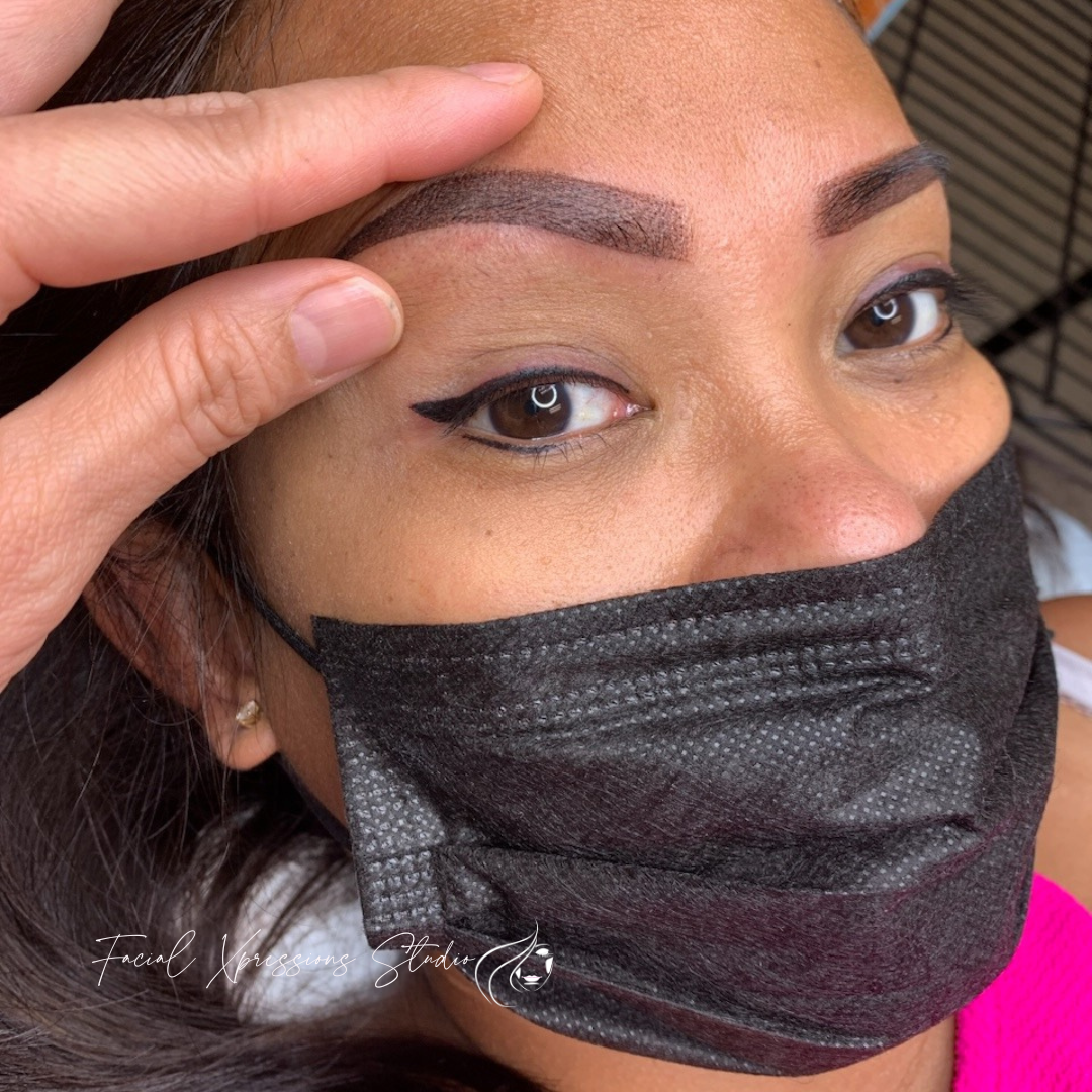 A woman wearing a black mask is touching her eyebrows