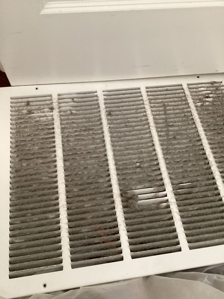 A white air vent with a lot of dust on it.