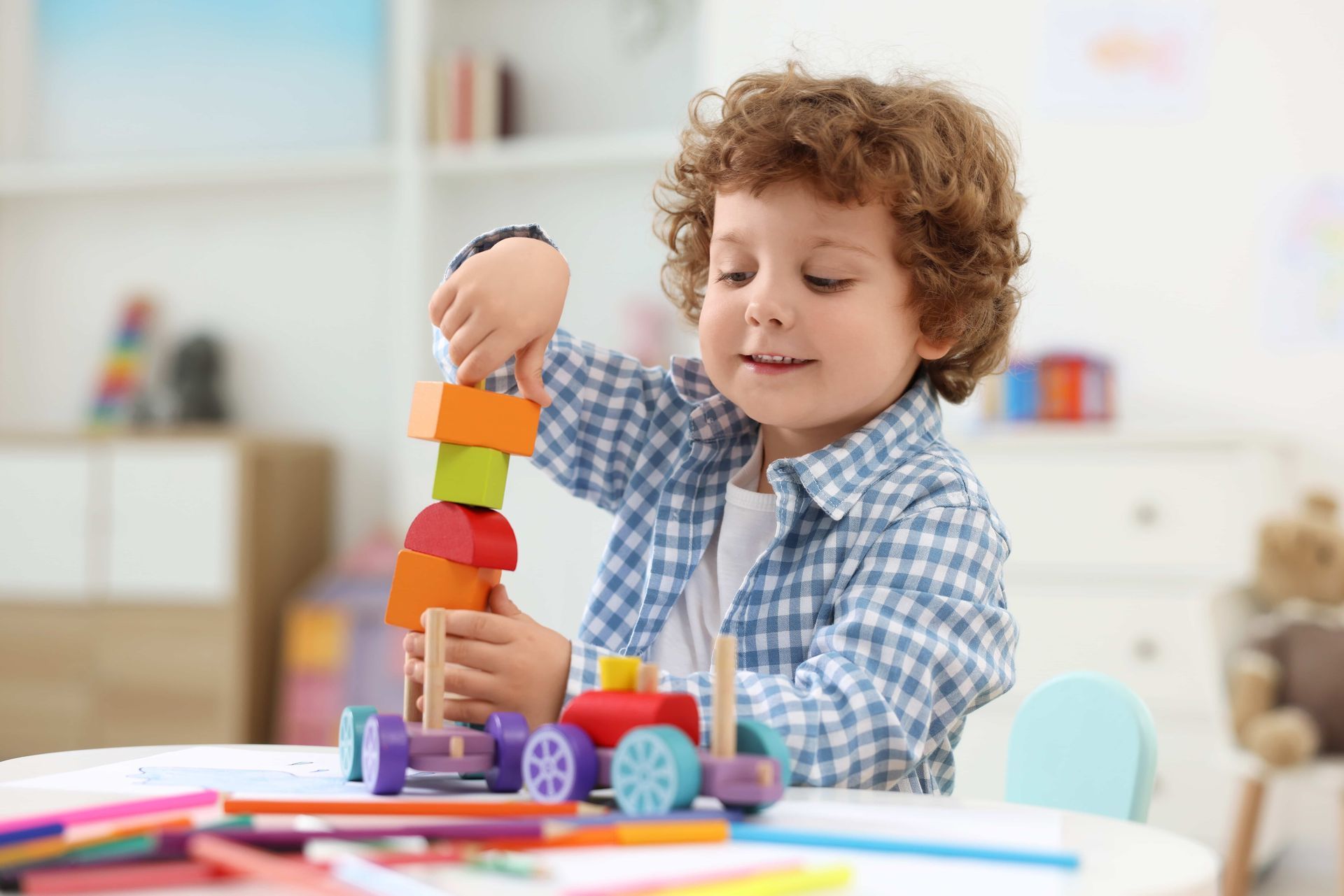 Boy with curly hair building a tower with colorful wooden blocks at a table.
